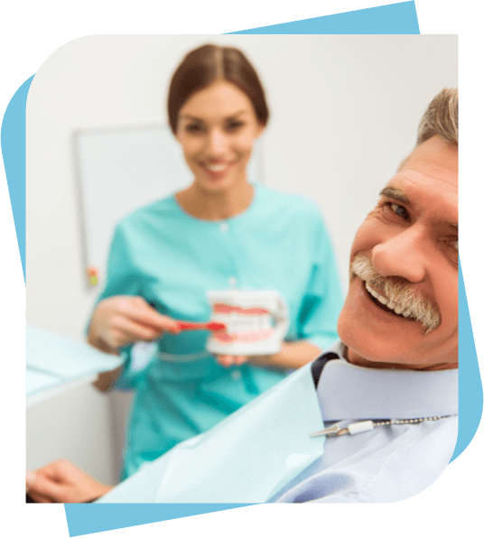 Middle aged man smiling while the dentist shows proper brushing techniques on a model in the backgorund.