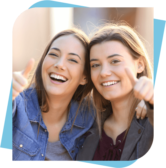Two young woman give a thumbs up while smiling