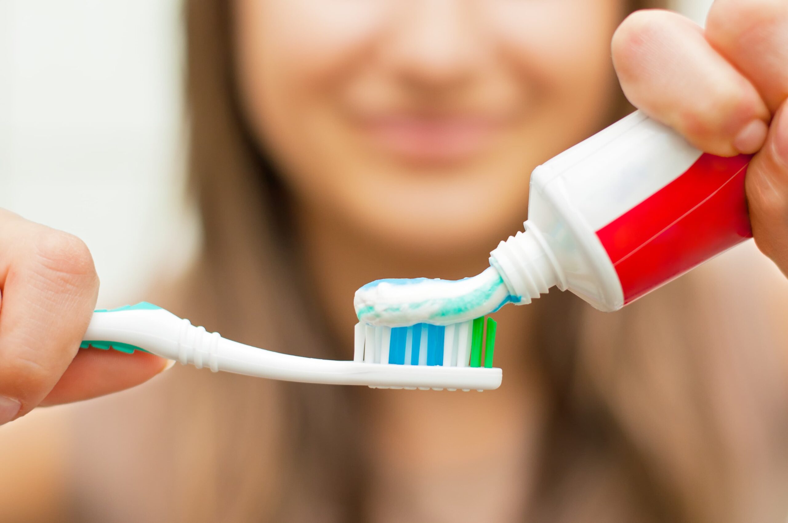 A woman smiles as she puts toothpaste on a manual toothbrush.