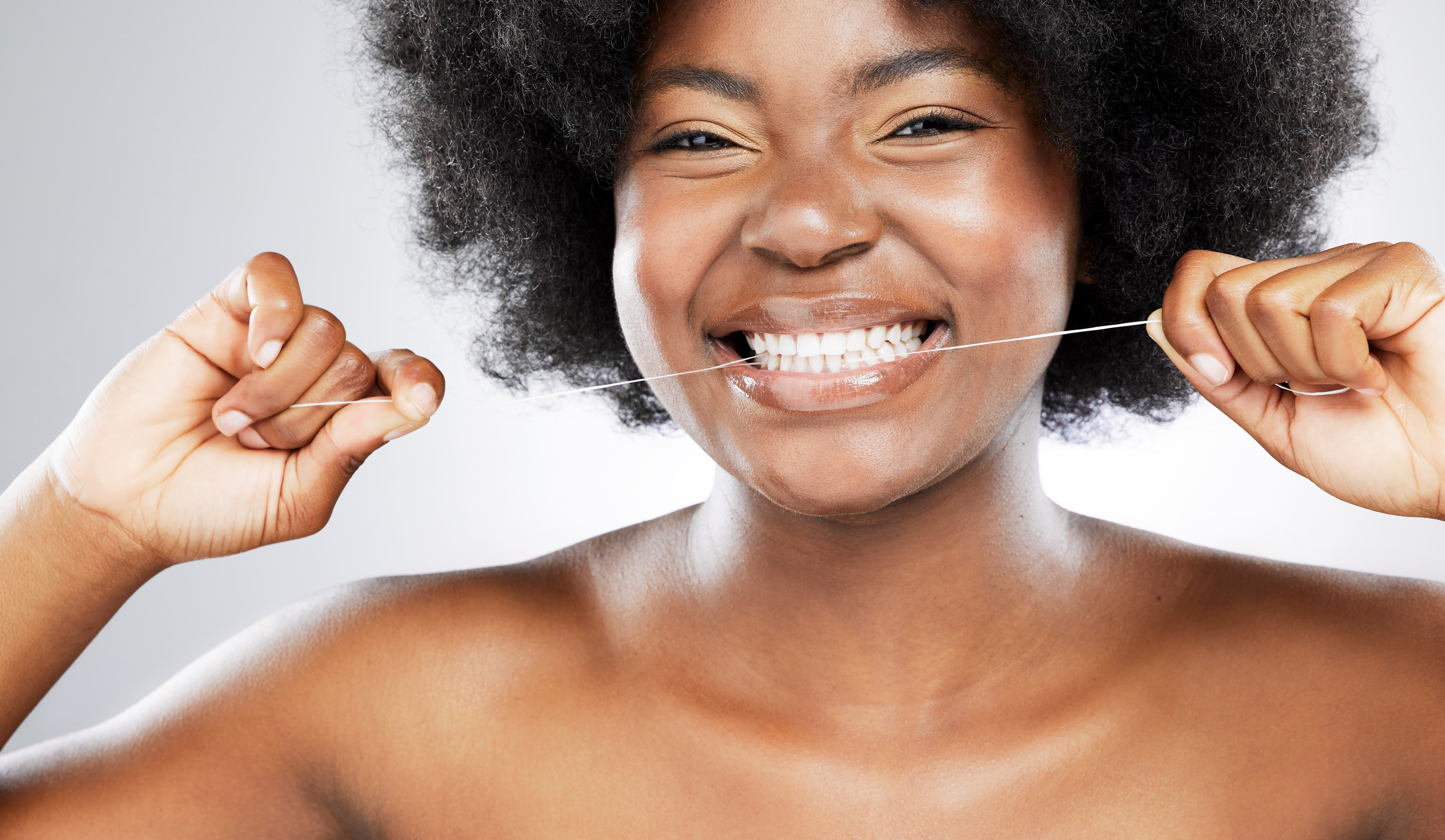 A woman smiles while flossing her teeth.