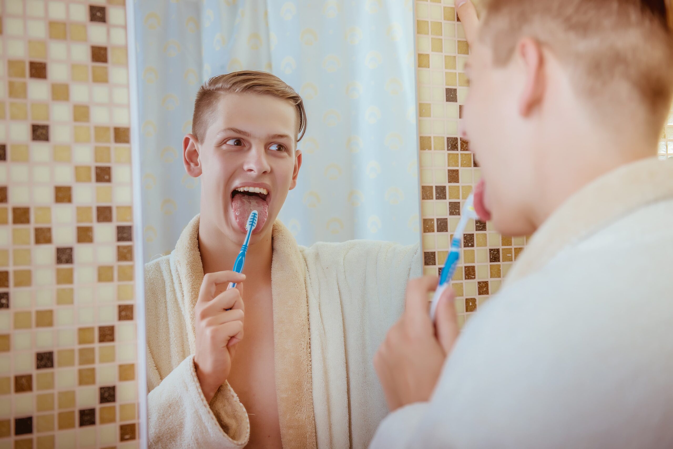A man brushes his tongue while looking into the mirror.